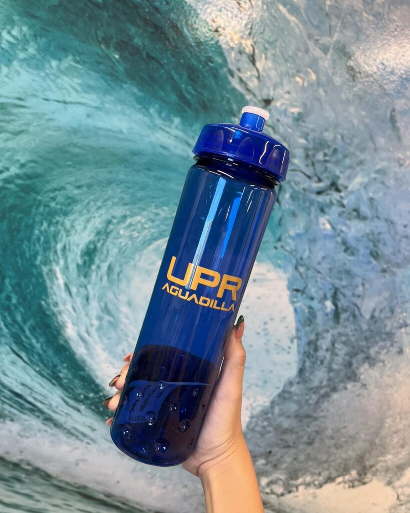 vaso plástico color azul personalizado con letras amarillas con el logo de UPR Aguadilla, el fondo es una ola de mar