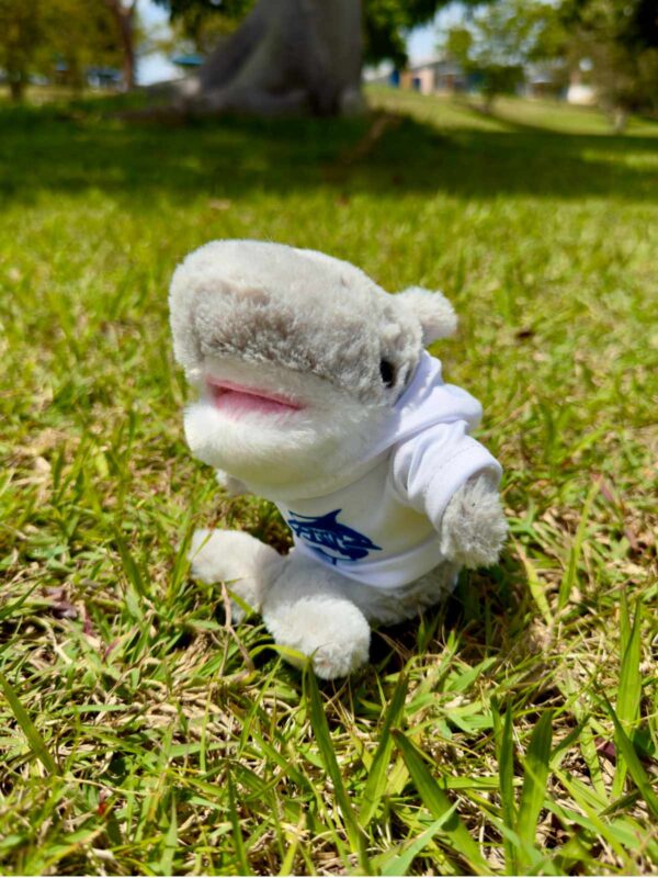 peluche en forma de tiburón con camisa blanca con logo de tiburón en color azul