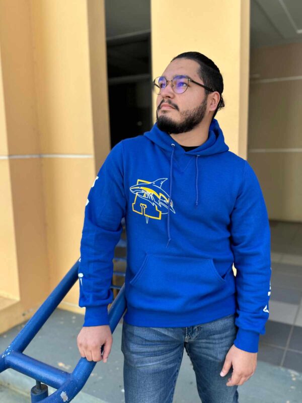 joven varón con sudadera azul con logo en el pecho de tiburón con A