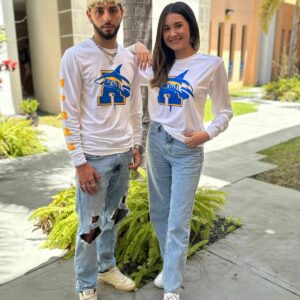 pareja de jóvenes modelando playera blanca con logo de tiburón y letra A en azul y amarillo