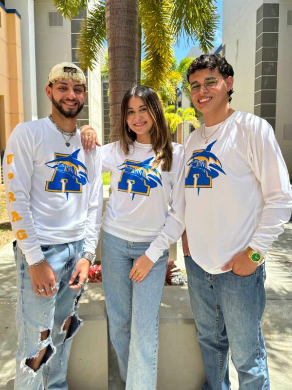 tres jóvenes modelando playera blanca con logo de tiburón y letra a en azul y amarillo