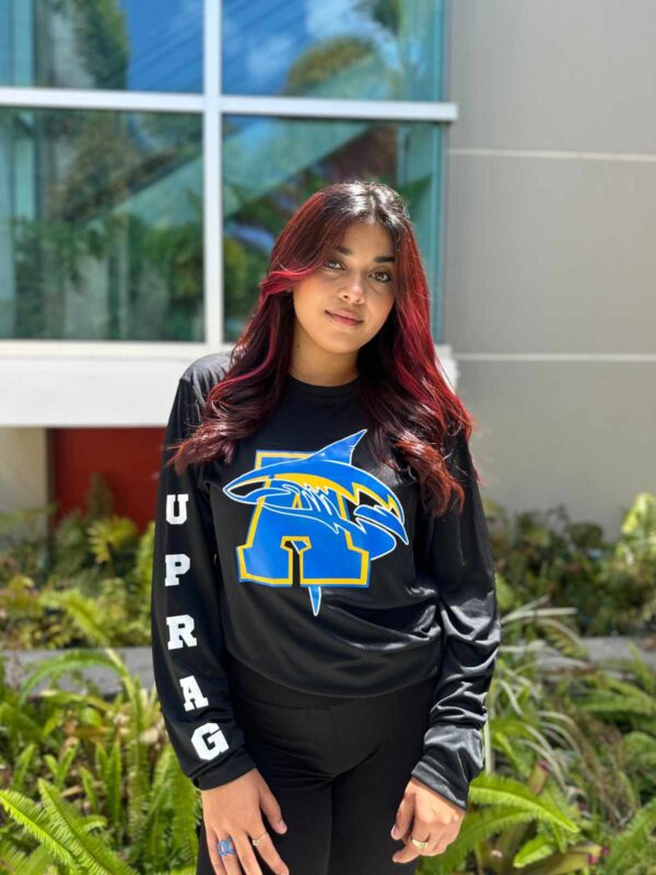 joven dama modelando playera negra con logo de tiburón y letra A en color azul y amarillo en la manga letras UPRAG