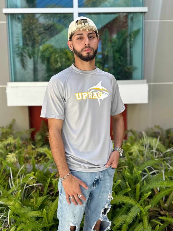 joven varón modelando camisa color gris con logo de UPRAg con tiburón en color blanco y amarillo