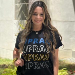 joven mujer modelando tshirt color negra con siglas UPRAG repetidas de forma vertical en colores azul y amarillo