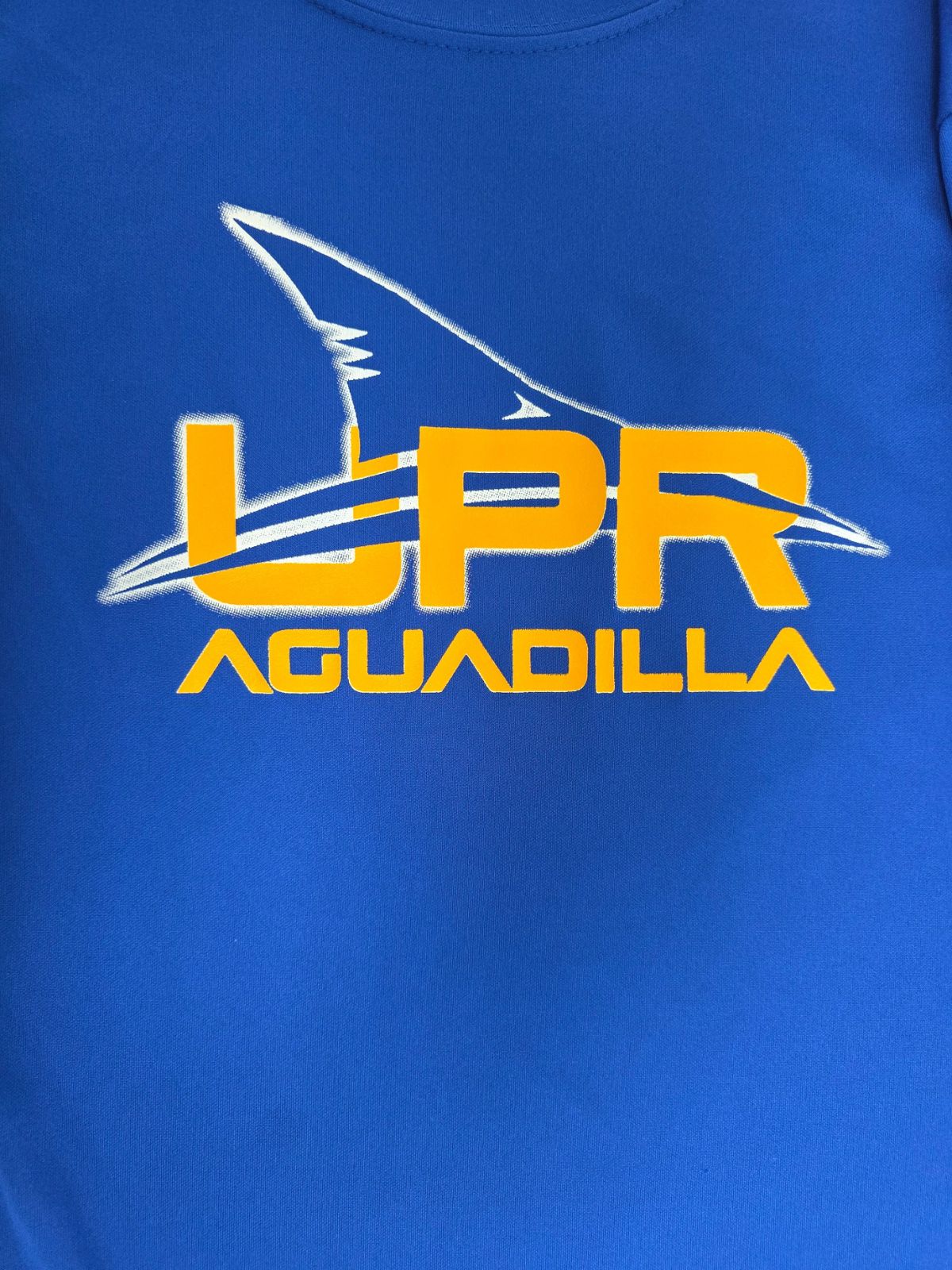 Estampado UPR Aguadilla en amarillo con silueta de tiburón sobre camiseta azul royal