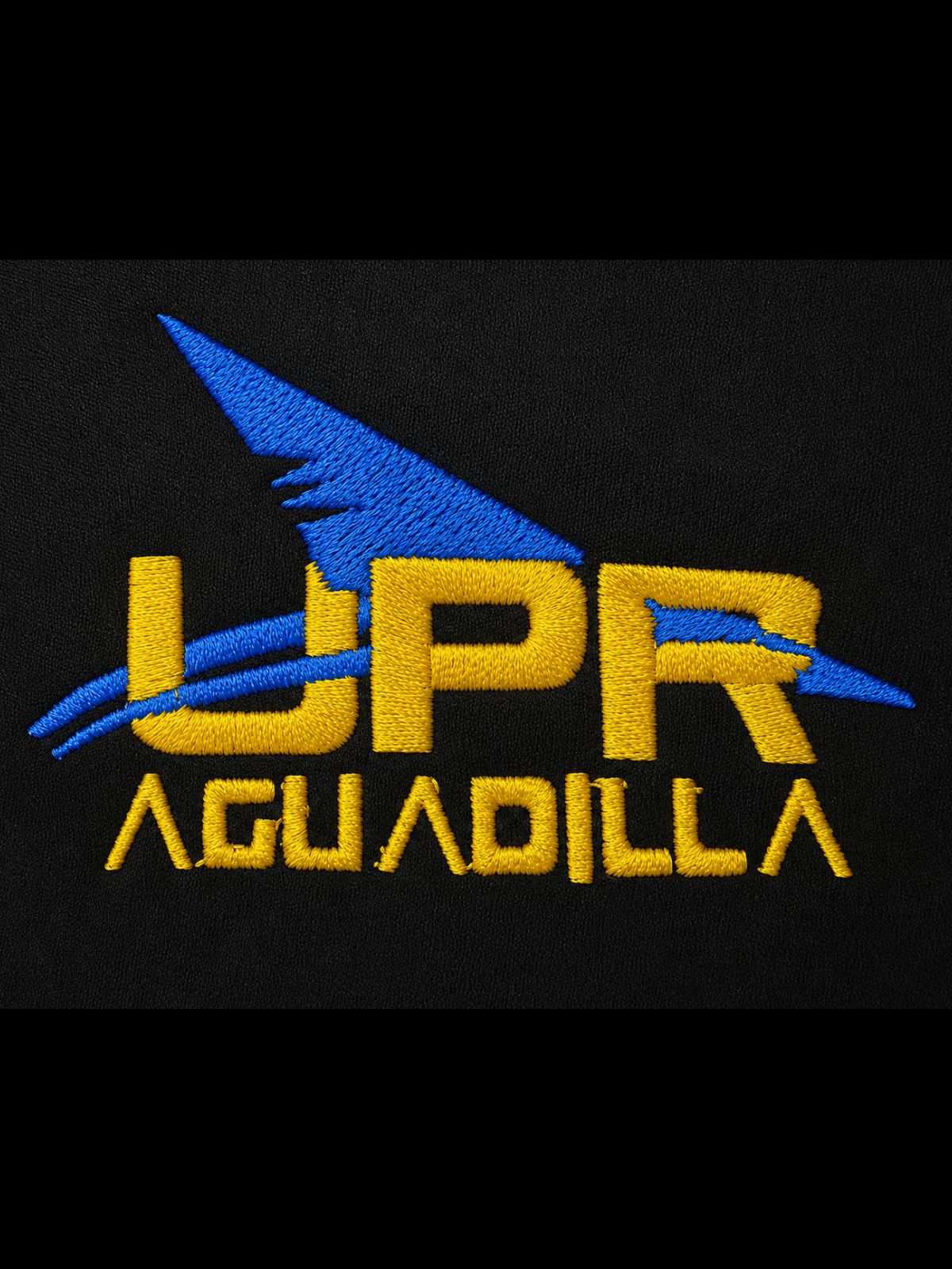 logo bordado institucional UPR Aguadilla en amarillo con aleta de tiburón en azul royal entrelazada en las letras UPR sobre una fondo negro